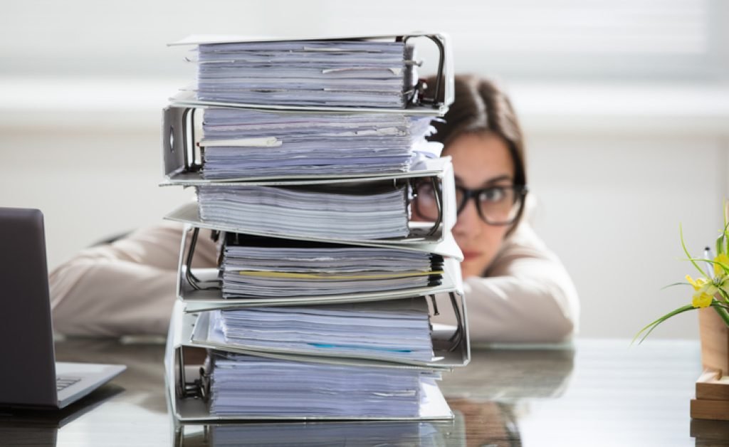 Close-up Of A Businesswoman Hiding Behind The Stack Of Folders On Desk At Workplace